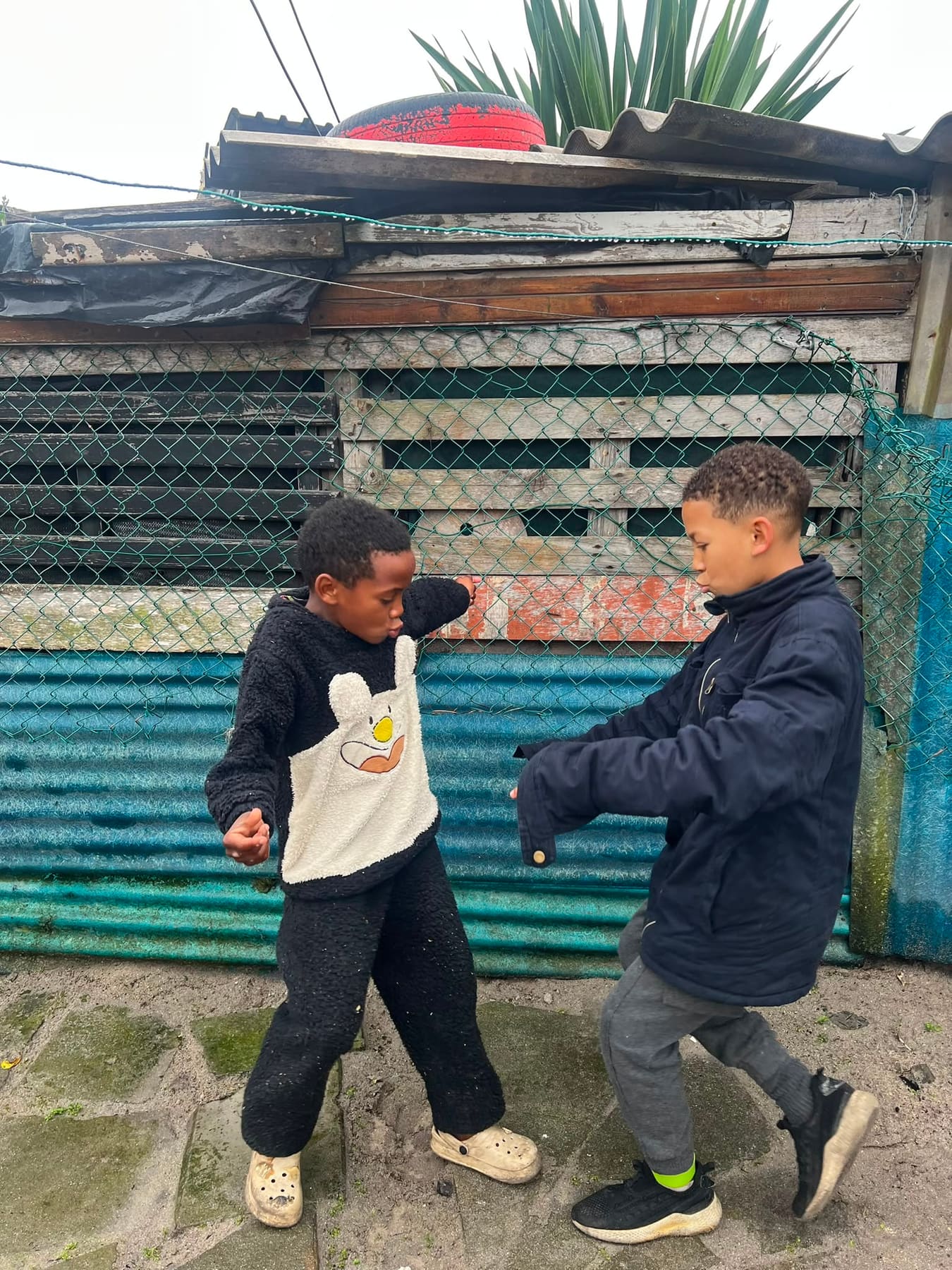 Two boys arm in arm against a whitewashed wall